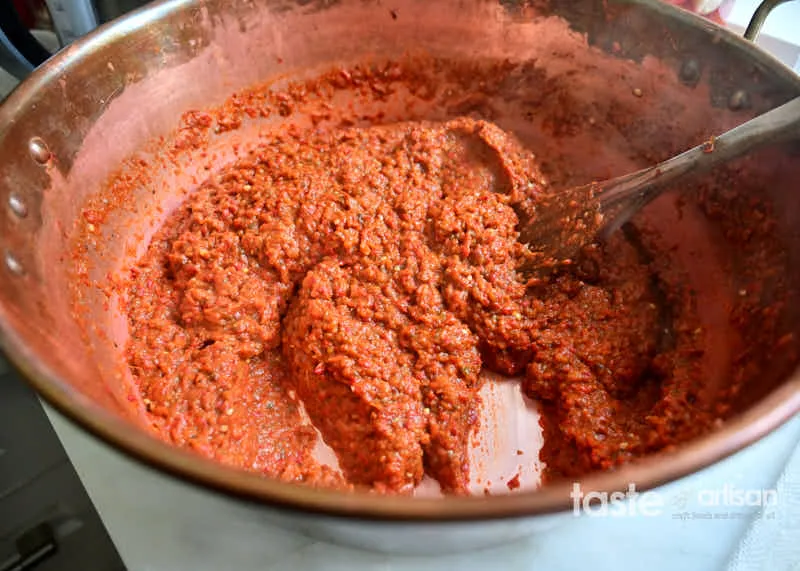 Ajvar, nach traditionellem Ajvar Rezept zubereitet, kocht in einer breiten Marmeladenpfanne auf einem Herd.