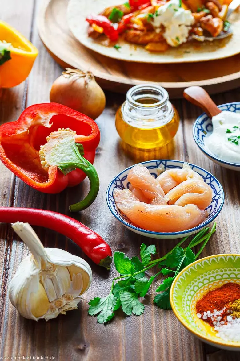 Alle frischen Zutaten für das Fajitas Rezept: Hähnchen, bunte Paprika, Zwiebeln, Limetten und Gewürze bereit zur Zubereitung