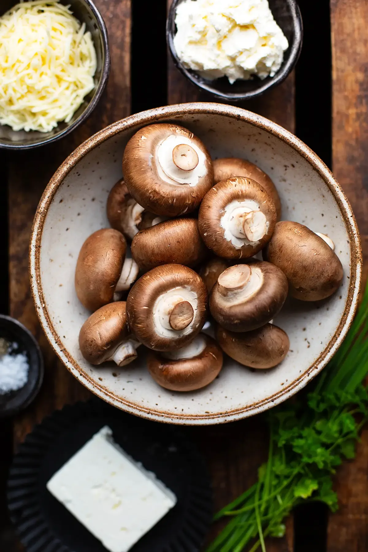 Alle frischen Zutaten für die vegetarisch gefüllten Champignons: braune Champignons, Feta, Frischkäse, geriebener Käse, frische Kräuter wie Schnittlauch und Petersilie, bereit zur Zubereitung.