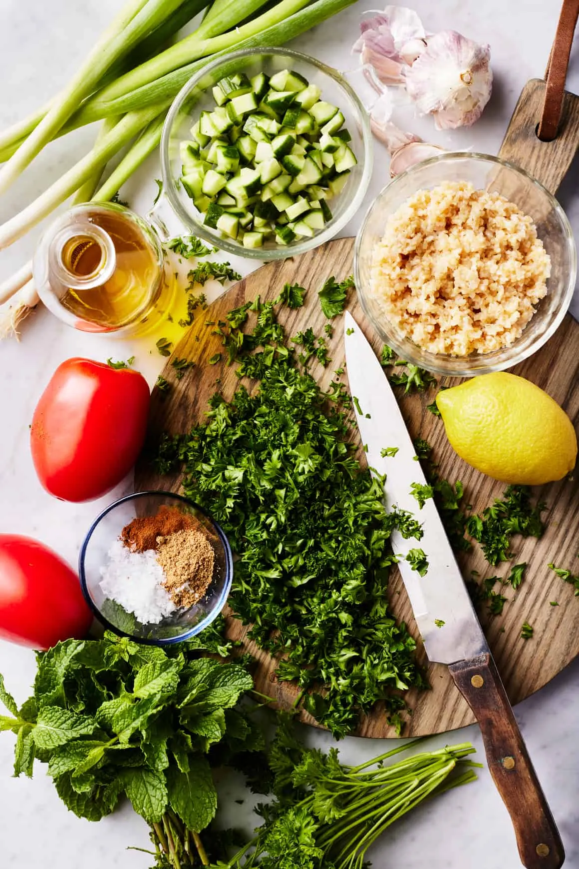 Alle Zutaten für den Tabouleh Salat: frische Kräuter, Gemüse, Bulgur und Gewürze auf einem Holztisch