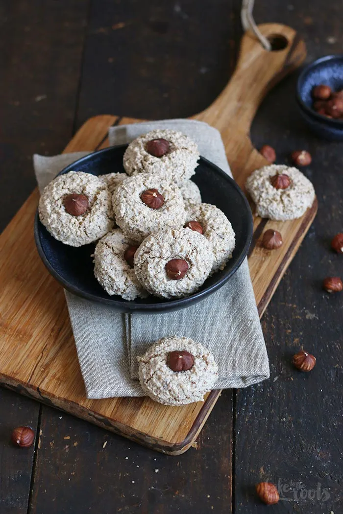 Alle Zutaten für Haselnussmakronen sind auf einem Holztisch arrangiert, einschließlich gemahlener Haselnüsse, braunem Zucker, Zimt, Eier und ganzer Haselnüsse.