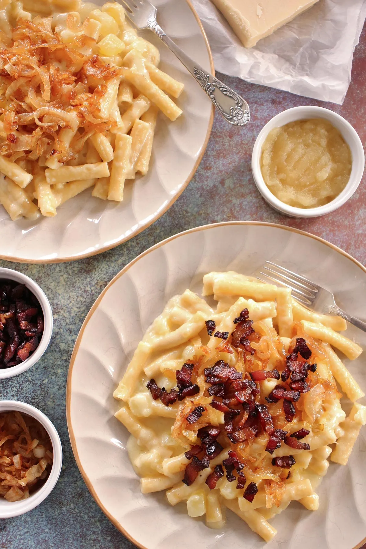 Älplermagronen auf zwei Tellern, garniert mit karamellisierten Zwiebeln und knusprigen Speckwürfeln