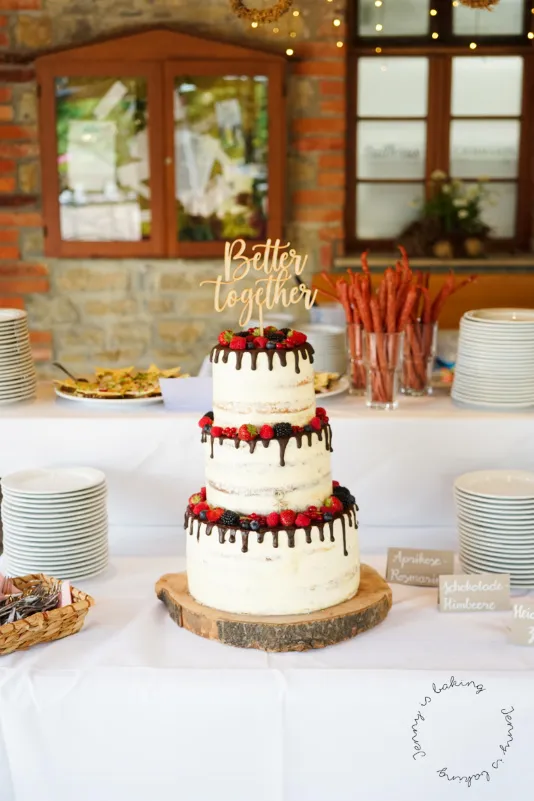 Alt-Text: Elegante dreistöckige Hochzeitstorte mit Schoko-Drip und Biskuitböden