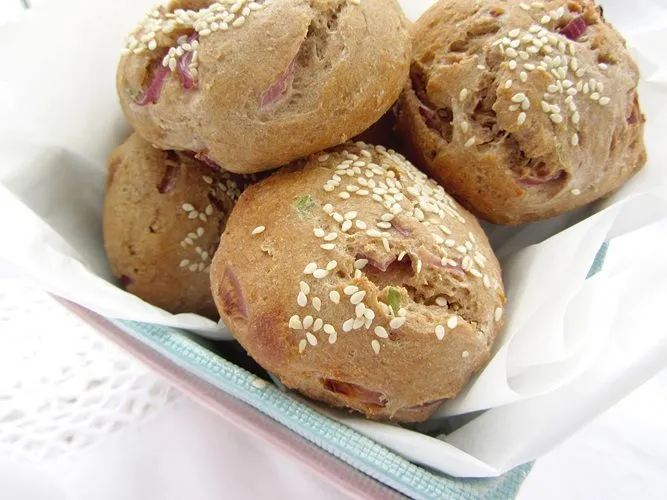 Alt text: Nahaufnahme von drei Dinkel-Buchweizen-Brötchen, die auf einem Holztisch liegen. Eines davon ist aufgeschnitten und zeigt die saftige Krume.