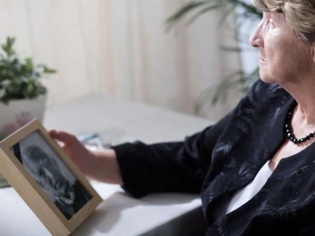 Ältere Frau schaut auf Bild eines verstorbenen Mannes