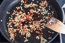 Angebratene Zwiebeln, Peperoni und Knoblauch in der Pfanne, die aromatische Basis für die Sauce des Erdnuss-Hähnchen-Topfs, typisch für viele afrikanische Rezepte.