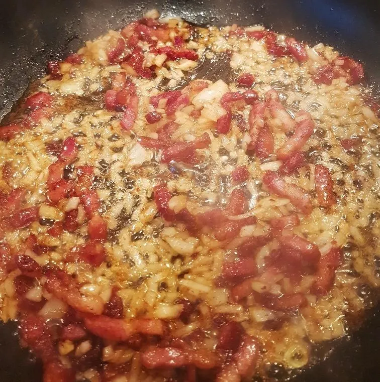 Angebratener Speck und Zwiebeln in einer großen Pfanne, bereit für die Zugabe von Knödeln und Braten