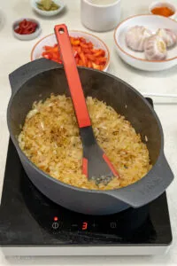 Angebratenes Gulaschfleisch mit Zwiebeln und Tomatenmark in einem Bräter, das Röstaromen entwickelt.