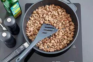 Angebratenes, krümeliges Hackfleisch in einer Pfanne, gewürzt mit Salz und Pfeffer, als Basis für den Taco Salat.