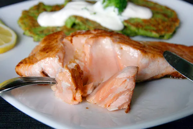 Angerichteter Lachs mit Brokkoli-Puffern, garniert mit Sauerrahm, frischer Zitrone und einer Petersilienbeilage