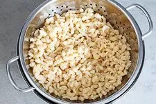 Anleitung Schritt 7: Eine dampfende Portion frisch gekochter Spätzle wird in eine vorgewärmte Servierschüssel gegeben, bereit zum Genießen.