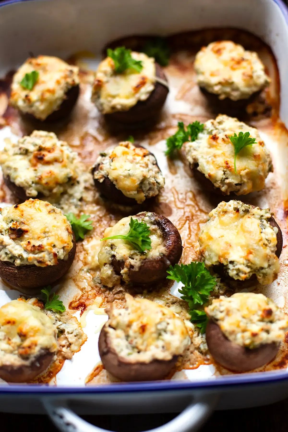 Appetitliche gefüllte Champignons mit Frischkäse und Feta, fertig gebacken und mit frischer Petersilie garniert, serviert in einer blauen Auflaufform.