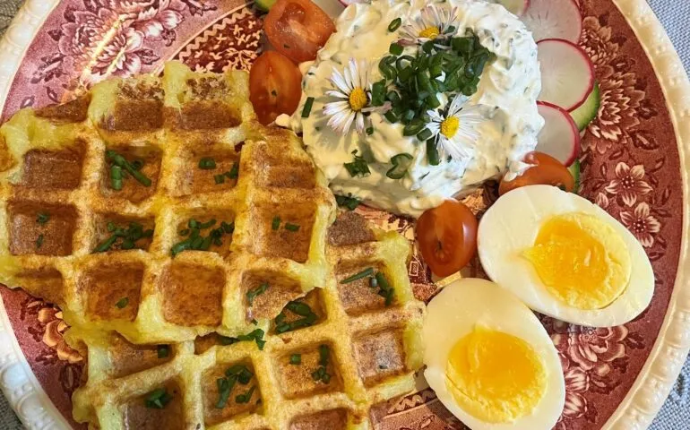 Appetitliche herzhafte Kartoffelwaffeln mit frischen Kräutern, serviert auf einem Holztisch im Freien