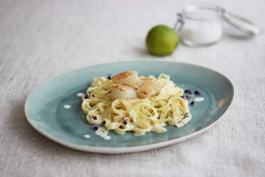 Appetitliche Präsentation von Tagliatelle mit Limettensauce und gebratenen Jakobsmuscheln, garniert mit frischer Petersilie.