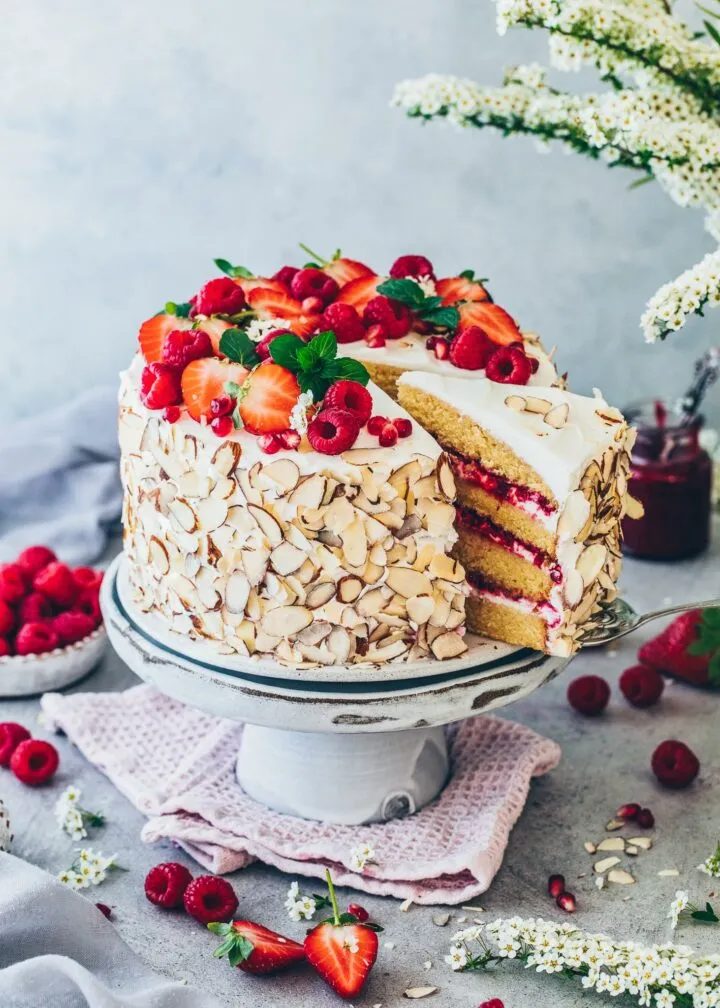 Appetitliche vegane Himbeer-Sahnetorte, dekoriert mit frischen Erdbeeren und Mandelsplittern.