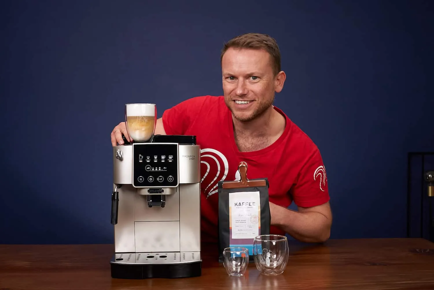 Arne Preuss lächelt und zeigt auf einen DeLonghi Magnifica Start Kaffeevollautomat