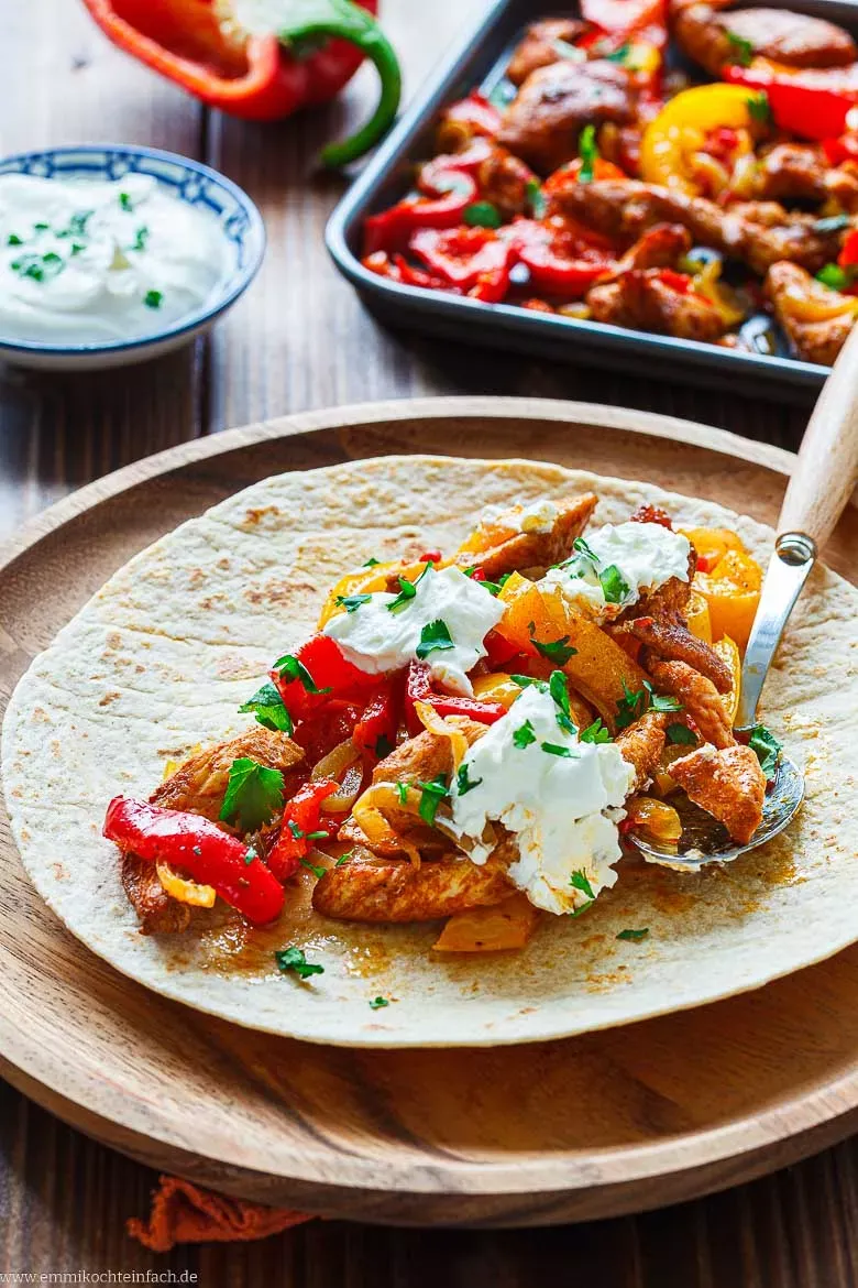 Aromatische Chicken Fajitas mit Paprika, frischem Koriander und einem Klecks Schmand servierfertig in Weizentortillas