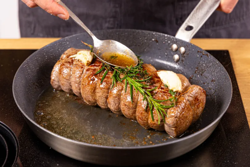 Aromatische Kräuter und Knoblauch zum angebratenen Rinderfilet geben