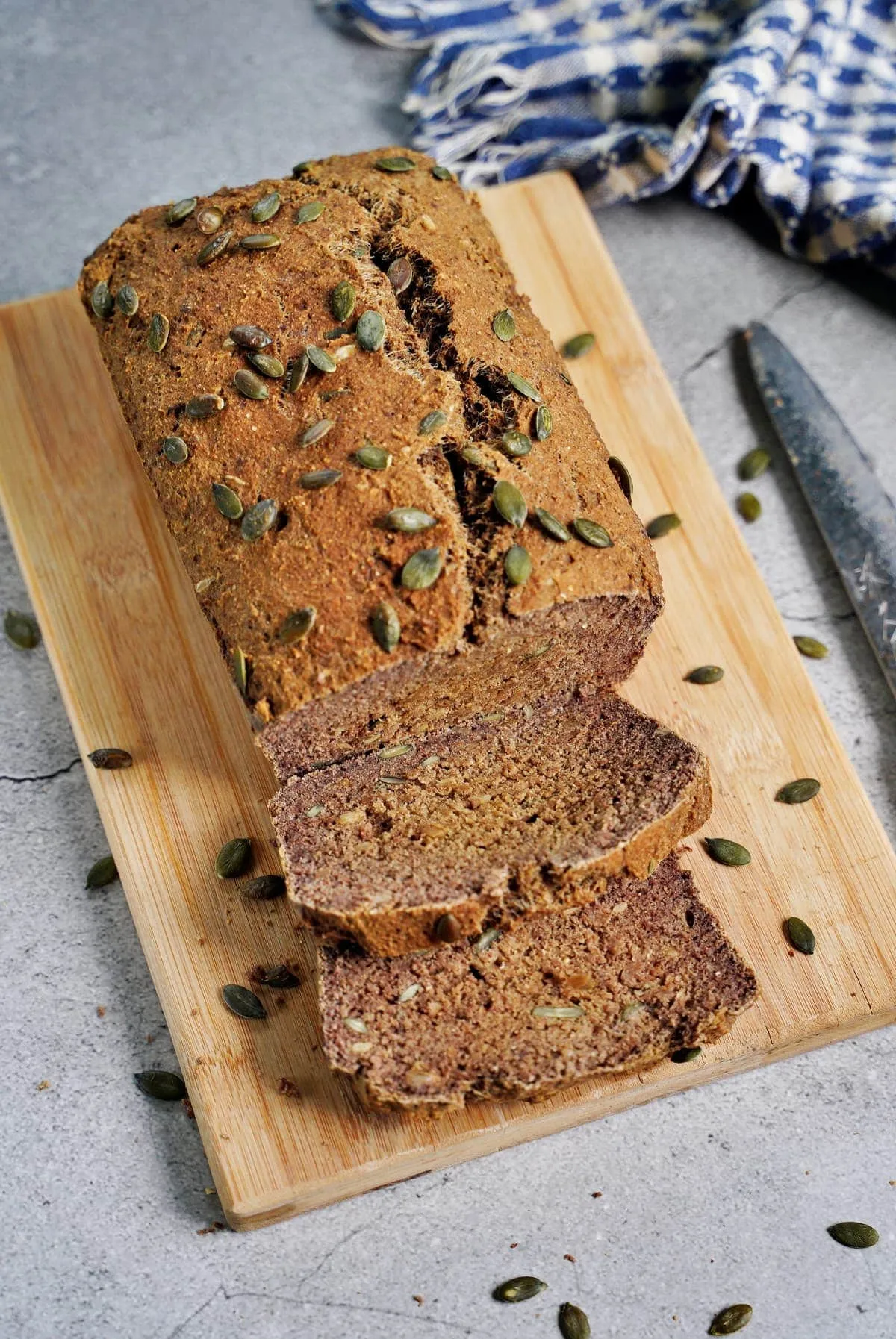 Aufgeschnittenes glutenfreies Eiweißbrot mit Kürbiskernen auf einem Holzbrett, die feine Textur enthüllend.