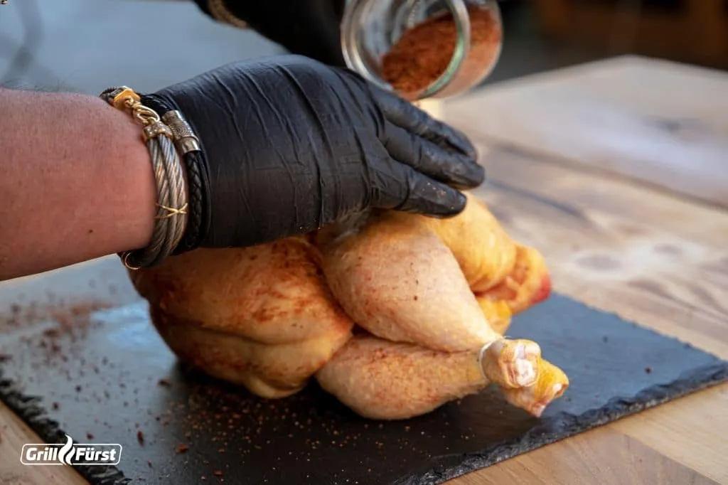 Auftragen des BBQ Rubs auf ein rohes Grillhähnchen vor dem Grillen