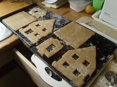 Ausgerollter Lebkuchenteig, aus dem mit Hilfe einer Schablone und einem Messer die einzelnen Teile eines Lebkuchenhauses ausgeschnitten werden.