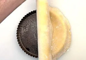 Ausgerollter Mürbeteig wird in eine Tarteform für Zwiebelkuchen gelegt