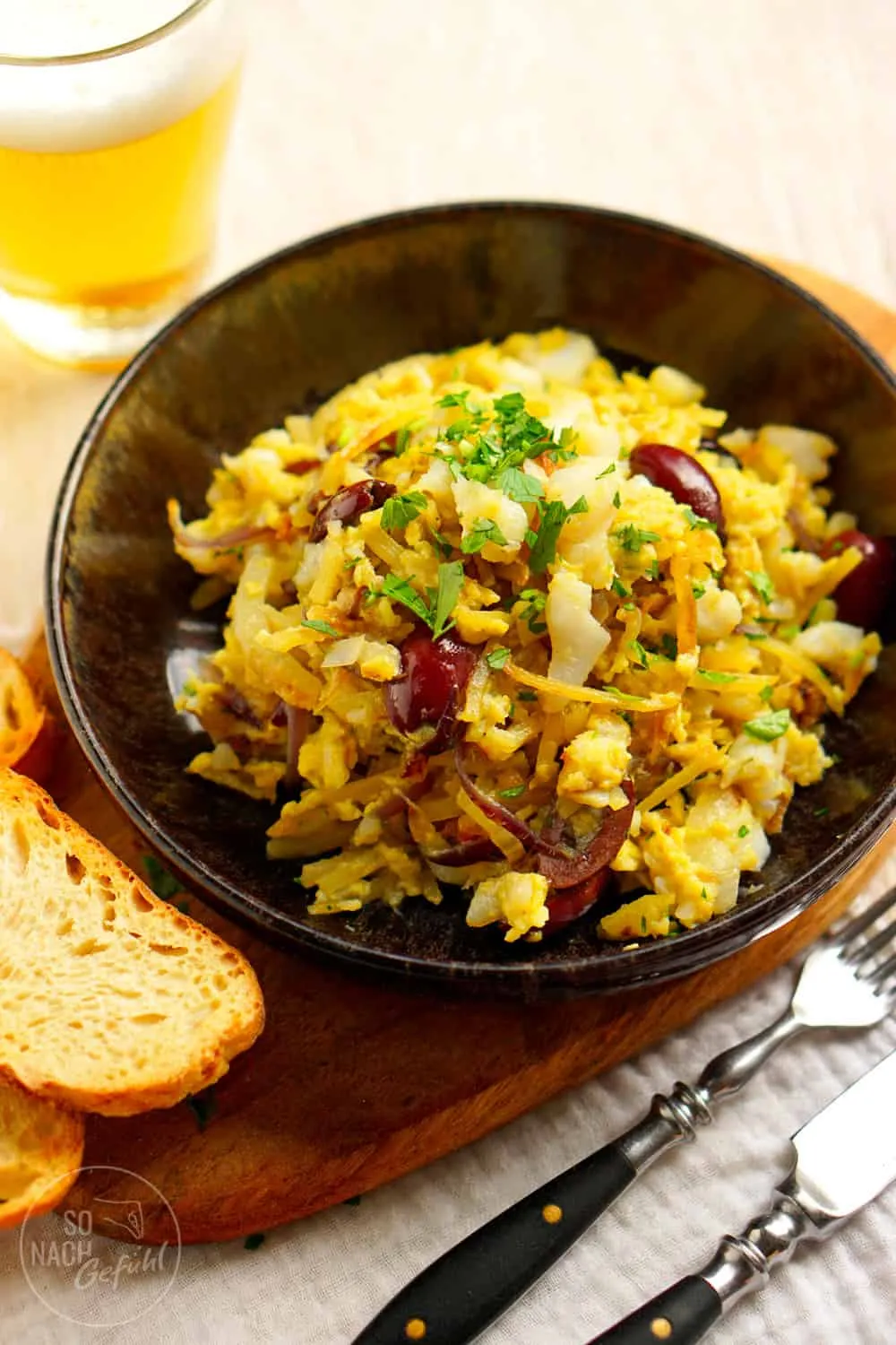 Bacalhau à Brás: Ein Teller portugiesischer Fischspezialität mit Kabeljau, Kartoffeln und Oliven, angerichtet auf einem Holztisch.