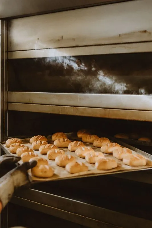 Bäcker holt Brötchen aus dem Ofen