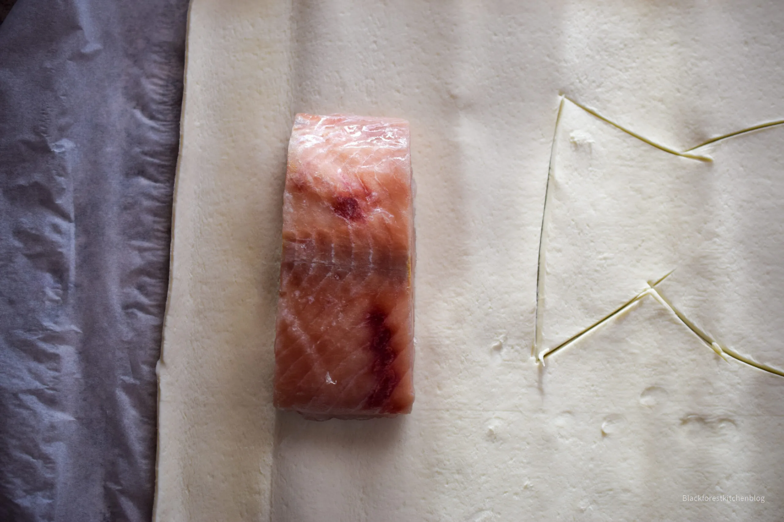 Blätterteig ausgebreitet mit einem Stück Lachs und der Gemüsefüllung darauf, bereit zum Einschlagen und Backen