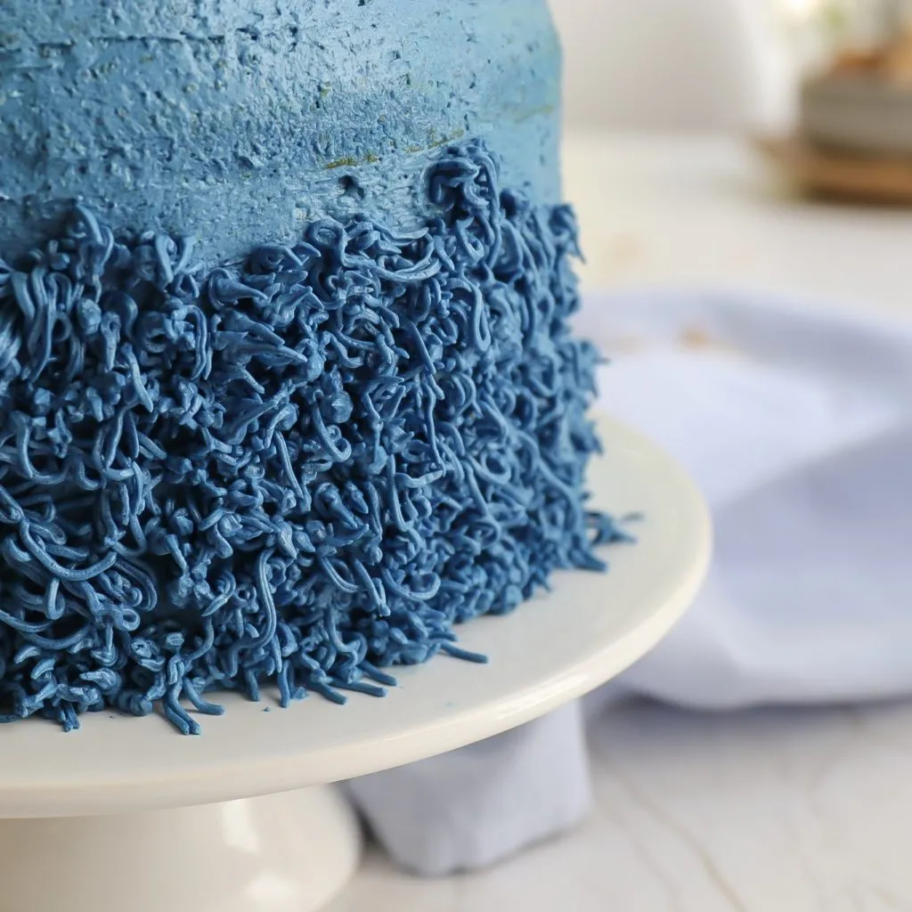 Blaues Krümelmonster-Fell mit einer Spritztülle auf den Geburtstagskuchen spritzen