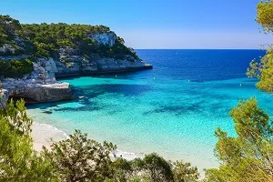 Bucht auf Menorca, Balearen, mit kristallklarem Wasser und Felsen, ein malerischer Ort für Strandurlaub im Juli.