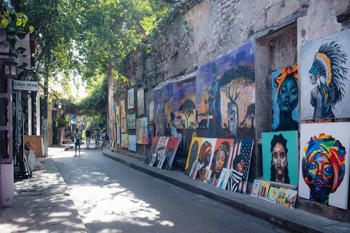 Bunte Gemälde an einer alten Hauswand in einer schmalen Gasse in einer Stadt mit verschiedenen Porträts und Landschaftsbildern entlang der Straße