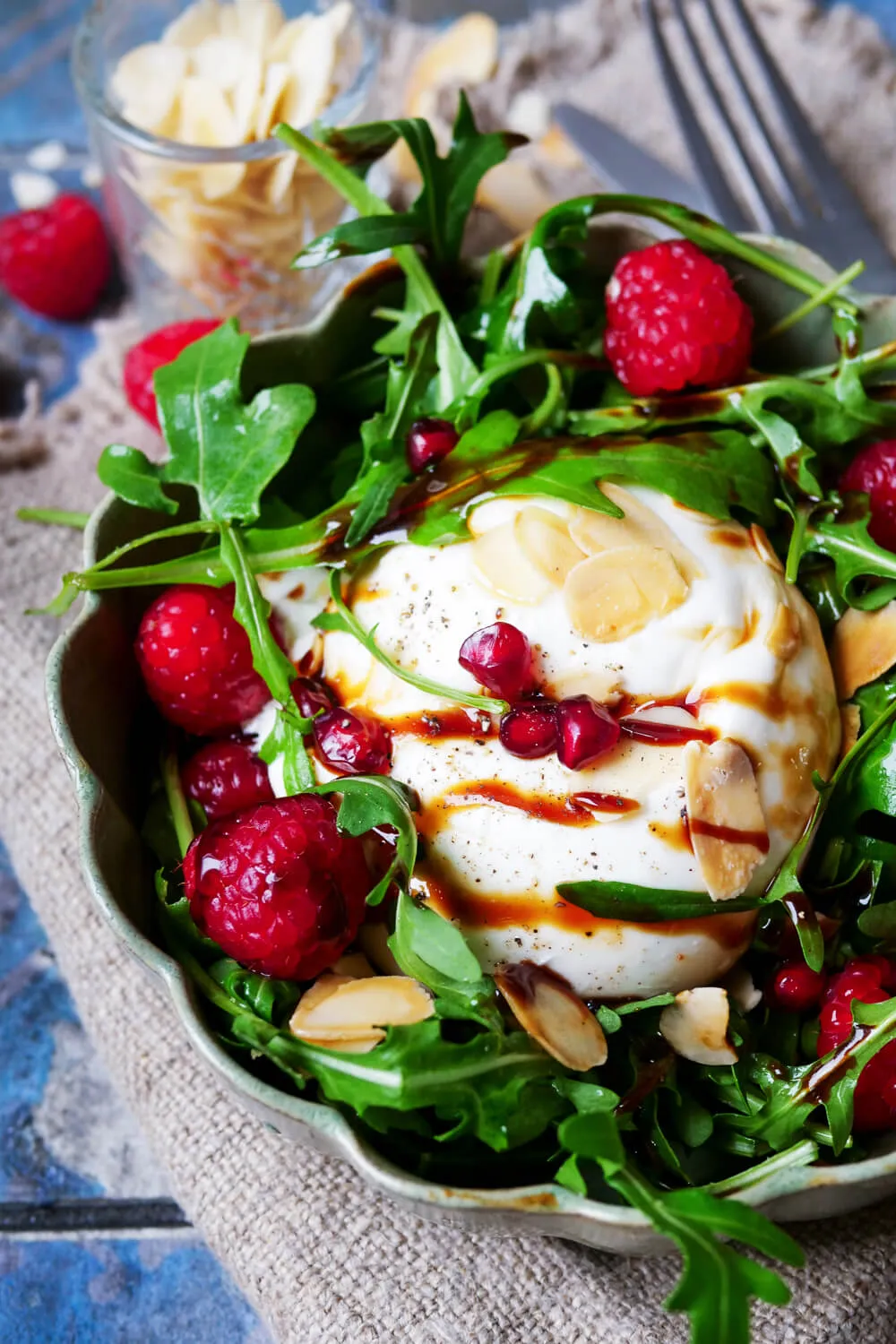 Bunter Burrata-Salat auf Rucola, garniert mit frischen Himbeeren und leuchtenden Granatapfelkernen.