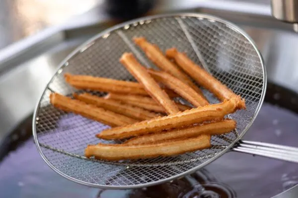 Churros werden mit Hilfe eines Siebes aus der Fritteuse gefischt.