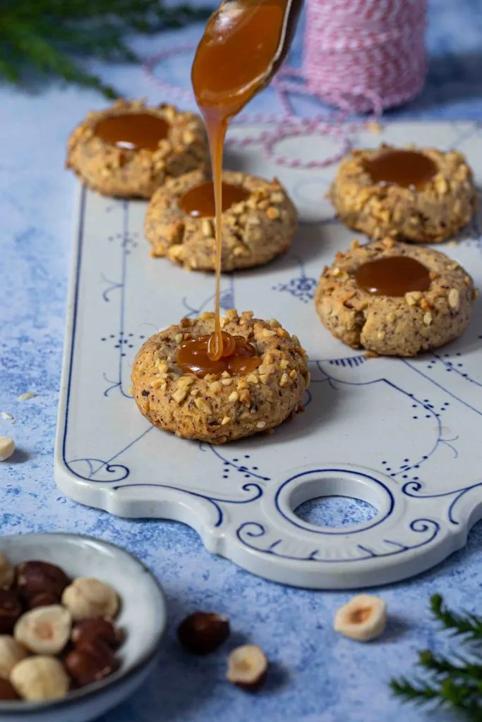 Close-up von Haselnuss-Engelsaugen, die mit einer glänzenden Karamellfüllung versehen sind, kunstvoll auf einem Holzbrett platziert