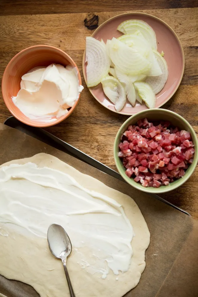 Crème fraîche als Basis für den Flammkuchenbelag gleichmäßig auf dem Teig verstrichen