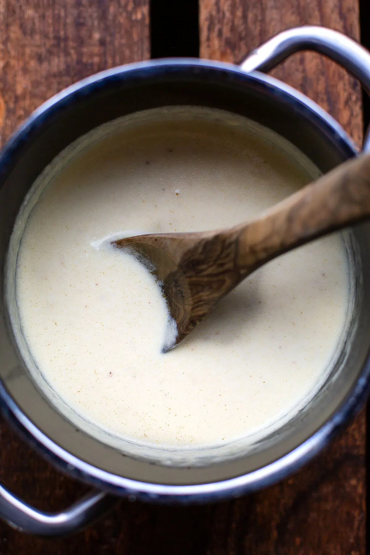 Cremige Käse-Sahne-Soße im Topf, gerührt mit einem Holzlöffel, bereit zum Servieren über Nudeln.