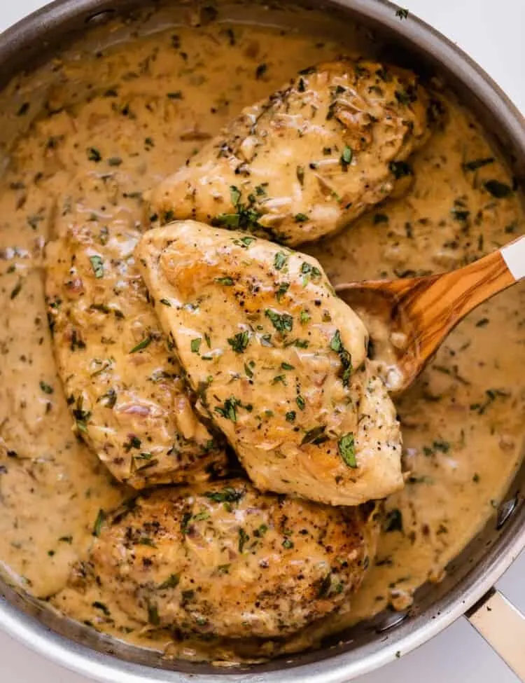 Cremiges Estragonhähnchen in einer Pfanne mit einem Holzlöffel.