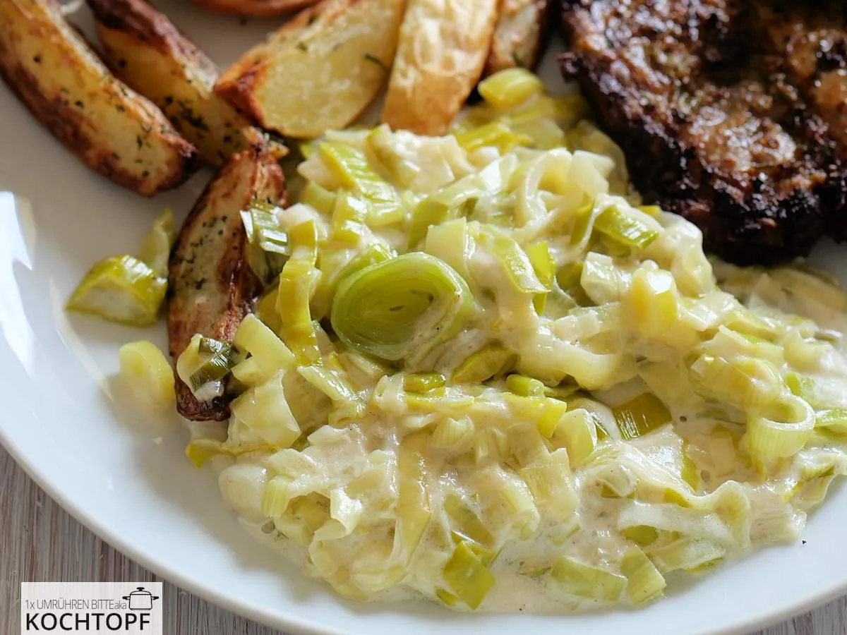 Cremiges Lauchgemüse als Beilage zu Kartoffel-Wedges und Nackensteak auf einem Teller angerichtet, appetitlich dampfend.