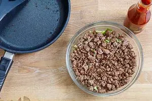 Das abgekühlte, gebratene Hackfleisch wird als zweite Schicht über den Eisbergsalat in die Salatschüssel gegeben.