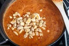 Das angebratene Hähnchenfleisch wird der cremigen Erdnuss-Tomaten-Sauce hinzugefügt und köchelt sanft im Topf – ein wesentlicher Schritt bei der Zubereitung dieses afrikanischen Rezepts.