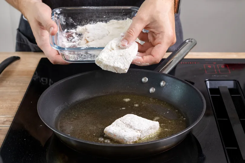 Das mehlierte Kabeljaufilet vorsichtig in die heiße Butterpfanne legen, um es goldbraun zu braten.