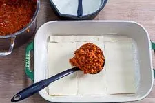 Das Schichten der Lasagneplatten und Verteilen der Bolognese Soße.