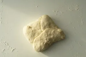 Der Baguette-Teig wird nach dem ersten Falten der linken Ecke weiter gefaltet, um die typische Baguette-Form zu erzielen.