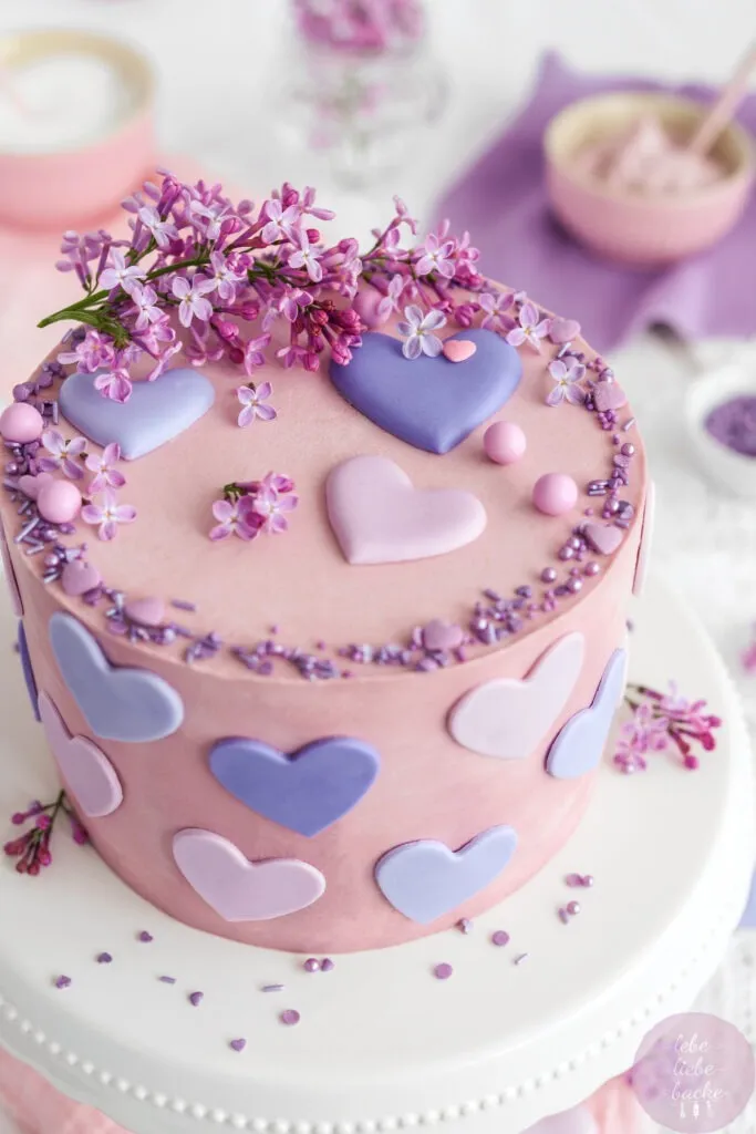 Detailansicht der Oberseite einer Käse-Sahne-Torte mit rosa Buttercreme und zarter Fliederblüten-Dekoration