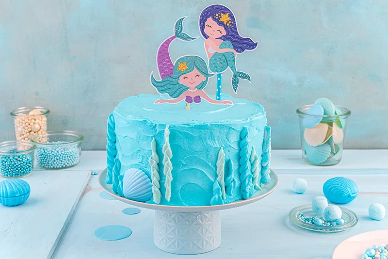 Detailansicht des Spritzbeutels beim Verzieren der Meerjungfrauen-Torte mit filigranen Korallen und Unterwasserpflanzen