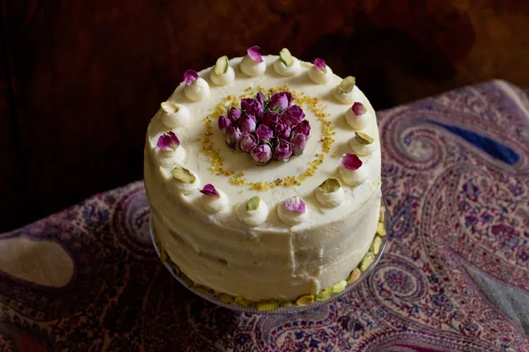 Detailaufnahme einer Pistazien-Rosen-Torte, mit frischen Rosenblättern und gehackten Pistazien verziert.