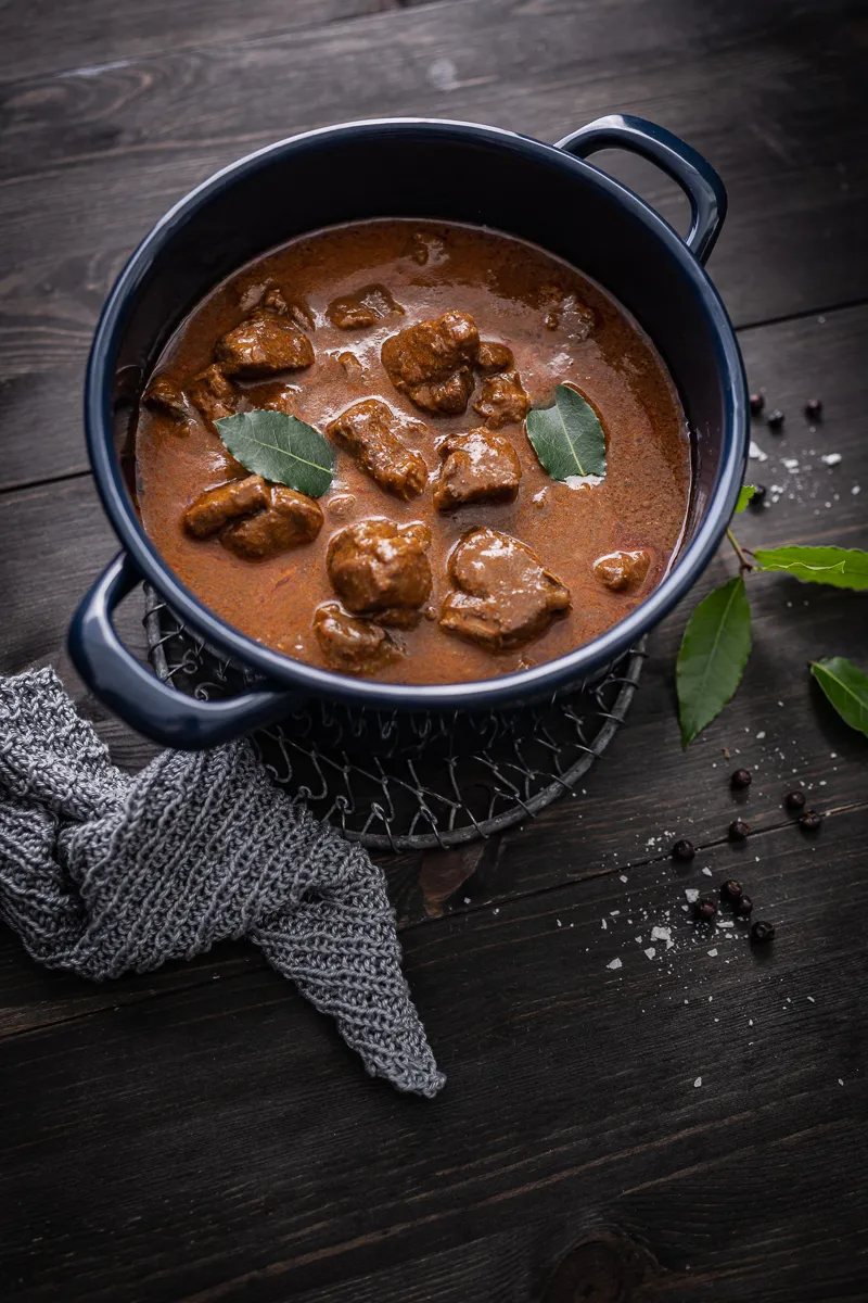 Detailaufnahme eines Tellers mit Wildschweingulasch und Haselnuss-Spätzle, garniert mit Preiselbeeren, die die Konsistenz des Fleisches und die Textur der Spätzle hervorhebt.