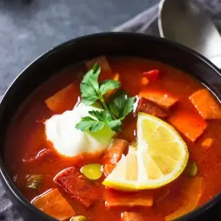Deutsche Soljanka Suppe in einer Schale, bestreut mit frischen Kräutern und einem Klecks saurer Sahne