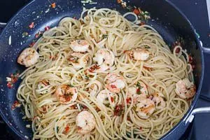 Die abgetropften Spaghetti mit den gebratenen Garnelen und der würzigen Soße vermengen, um sicherzustellen, dass jede Nudel gut bedeckt ist – ein Genuss, der auch in Deutschland geschätzt wird.